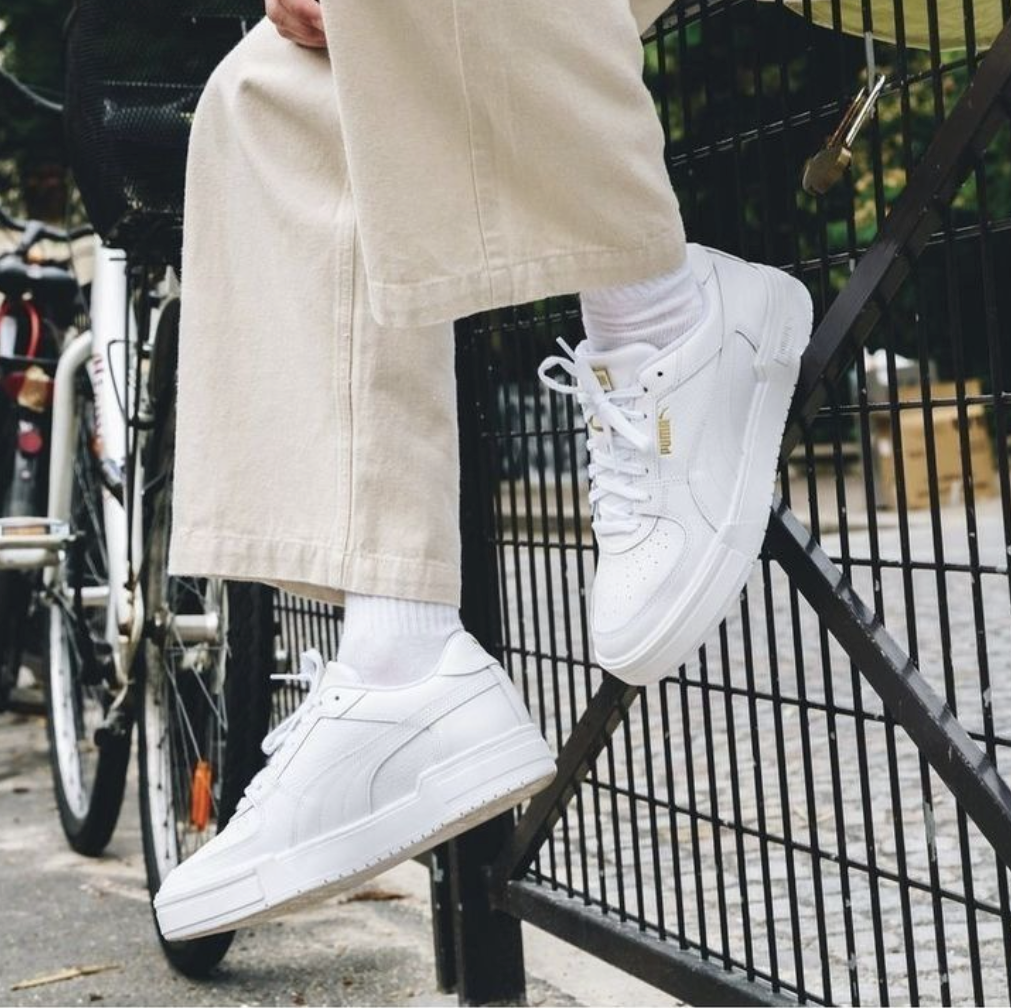 Mann sitzt auf schwarzem Zaun mit creme leinen Hose und weißen Puma Suede Sneaker