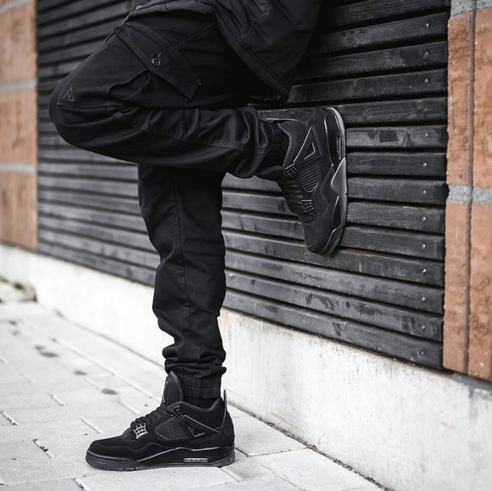 Schwarze Air Jordan 4 Black Cat mit schwarzer Hose in urbanen Hintergund 
