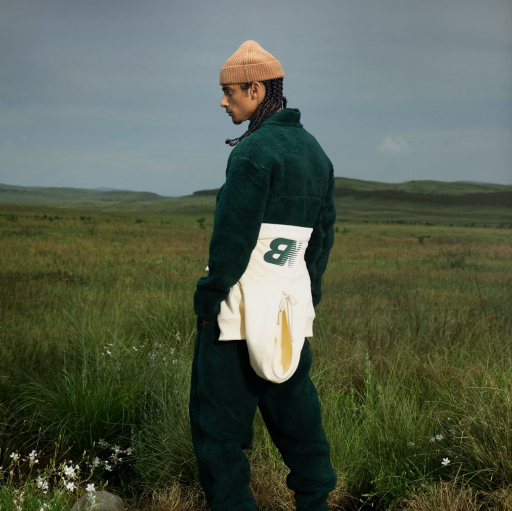 Mann mit umgebundener New Balance jacke in weiß mit grünem Outfit mit grüner Wiese im Hintergund