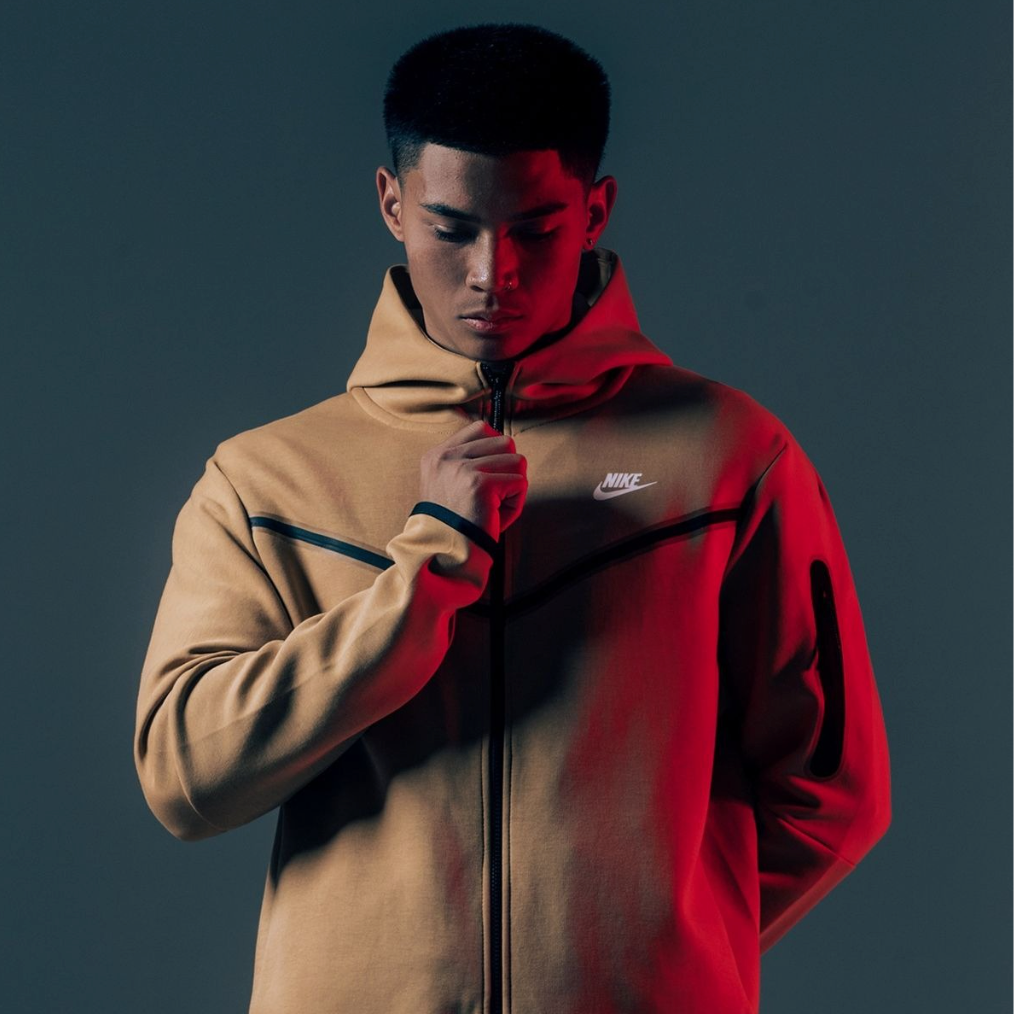 Mann in grauem Hintergrund mit braunem Nike Tech Jacke 