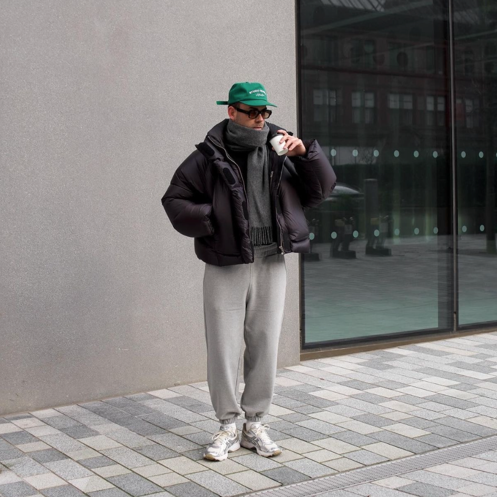 Asics Sneaker, graue Jogginghose und brauner Pufferjacke in urbanem Hintergund