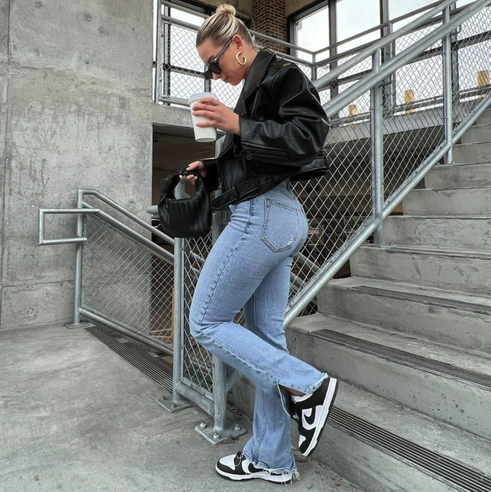 Frau in Treppenhaus eines Stadions mit Nike Dunk Low SB Panda und einer Lederjacke 