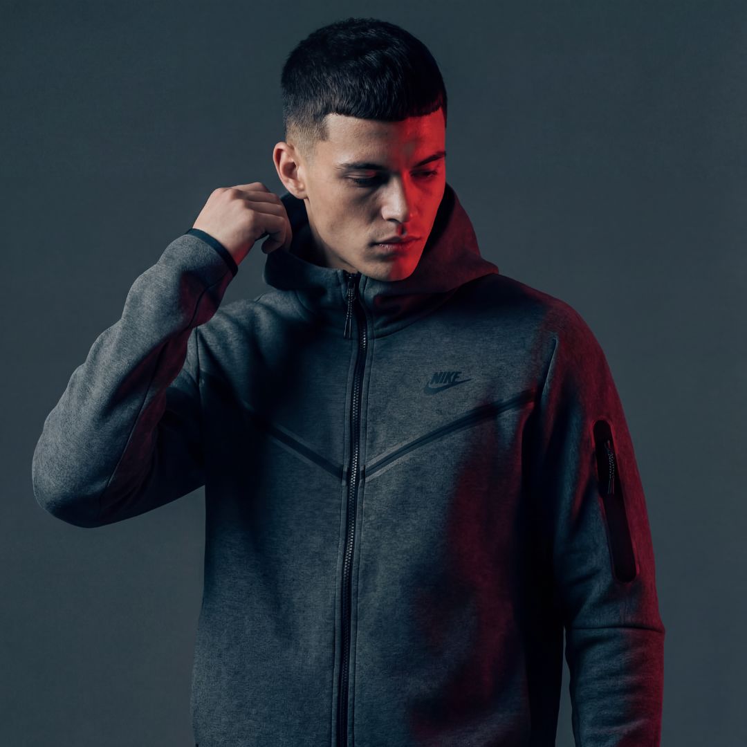 Mann in grauem Hintergrund mit schwarzer Nike Tech Jacke 