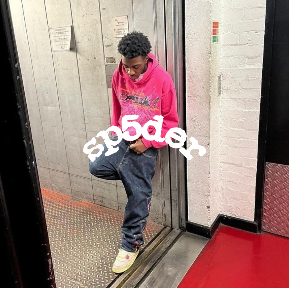 Sp5der Logo, Mann stehend in der Tür eines Aufzuges mit rosa Hoodie und blauer jeans