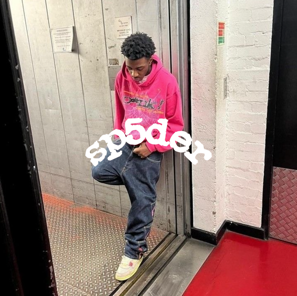 Sp5der Logo, Mann stehend in der Tür eines Aufzuges mit rosa Hoodie und blauer jeans