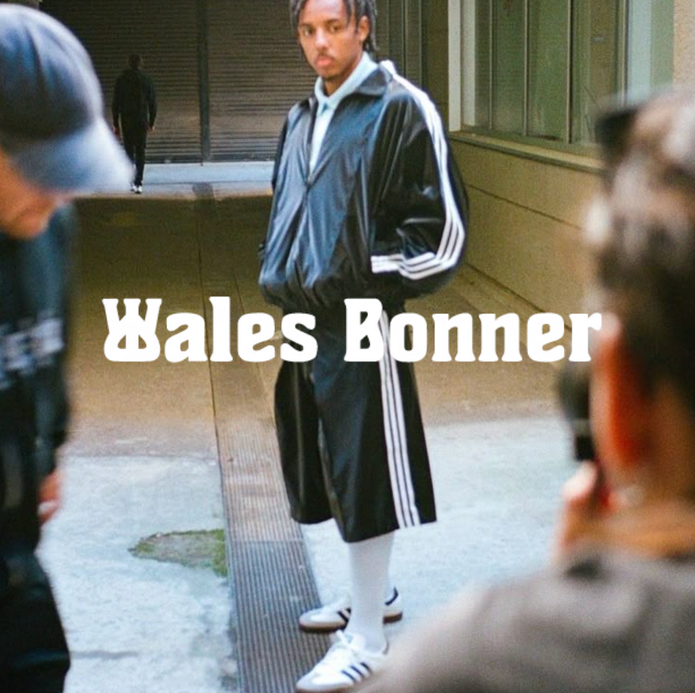 Person in einem retro-inspirierten Wales-Bonner-Trackset steht in einer urbanen Umgebung; im Vordergrund „Wales Bonner“-Schriftzug sichtbar.