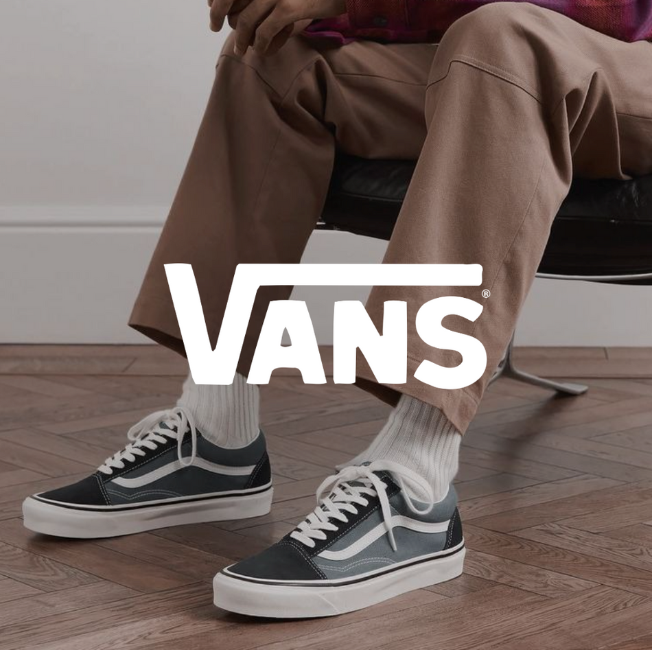 Person sitzt entspannt auf einem Stuhl und trägt klassische Vans Old Skool Sneaker in Schwarz-Weiß; Fokus auf Schuhe und lässigem Streetwear-Look.