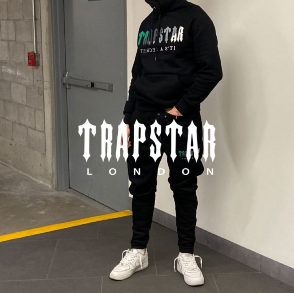 Trapstar Logo, Mann mit Trapstar Tracksuit und weißen Sneakern steht vor einem gebäude