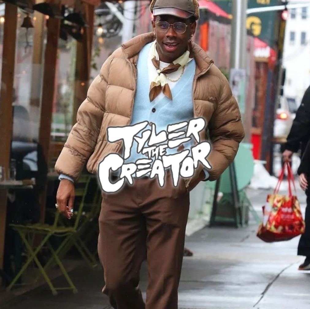 Tyler The Creator läuft in blauem sweater und brauner Jacke sowie Hose eine Straße entlang