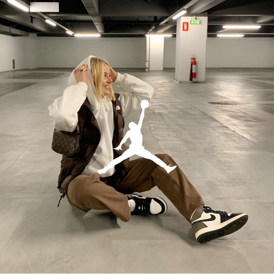 Jordan Logo, weibliches Model mit Air Jordan 1 Mocha und brauner Hose sitzend auf dem boden eines Parkhauses