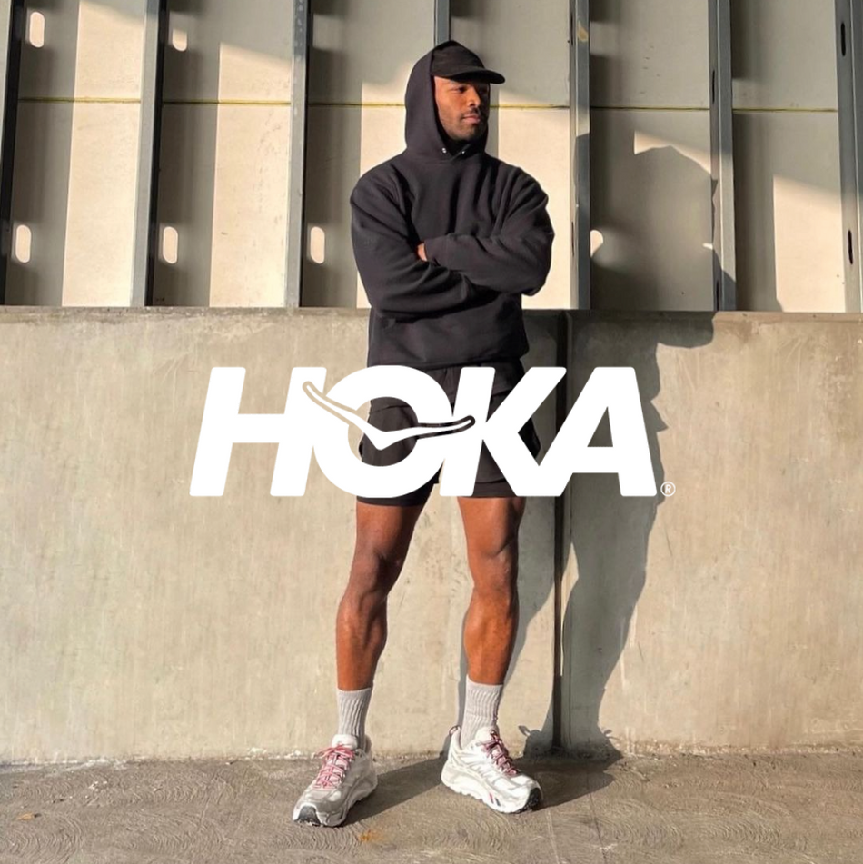 Hoka Logo mit einem Jogger mit Running Sneakern und schwarzem Sportoutfit stehend vor einem Gebäude