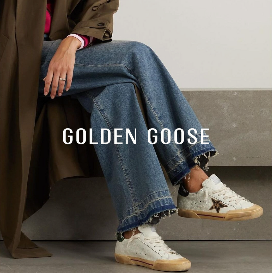 Golden Goose logo mit Frau in flachen cremefarbenen  Sneakern in blauer Jeans und grünem MantelSneakern 