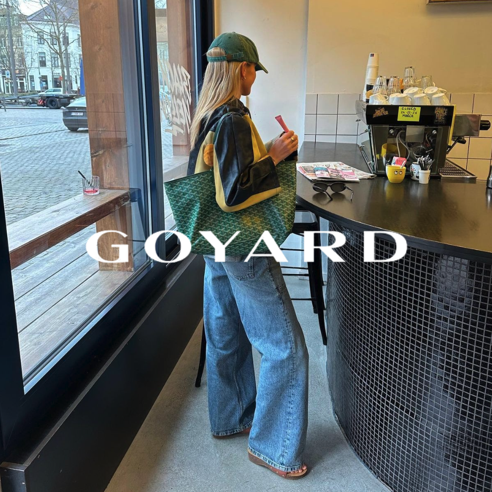 Goyard Logo, Frau mit grüner Cap und grüner Goyard Tasche über der Schulter in einem Cafe