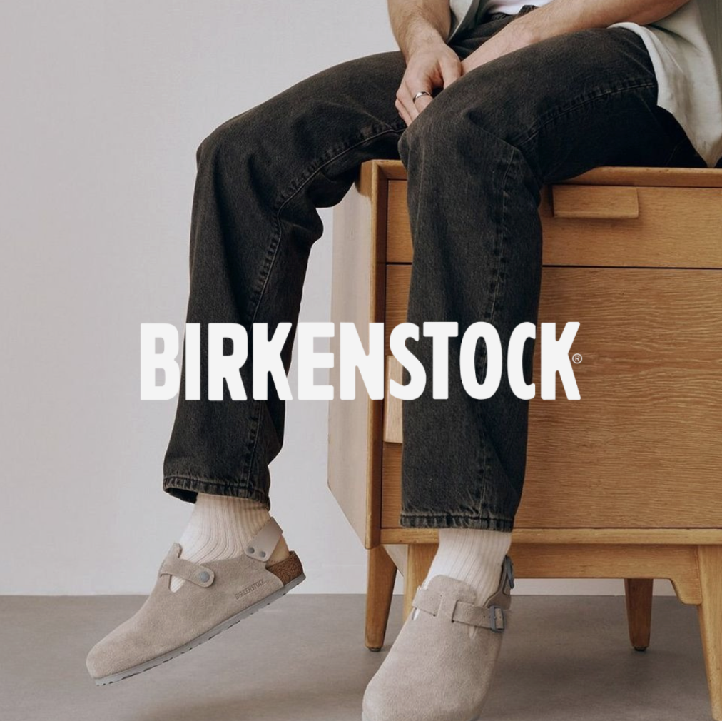 Mann sitz auf Komode mit grauen Birkenstocks und einer schwarzen Jeans