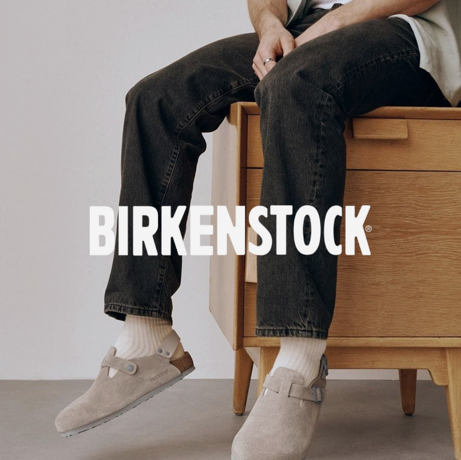 Mann sitz auf Komode mit grauen Birkenstocks und einer schwarzen Jeans