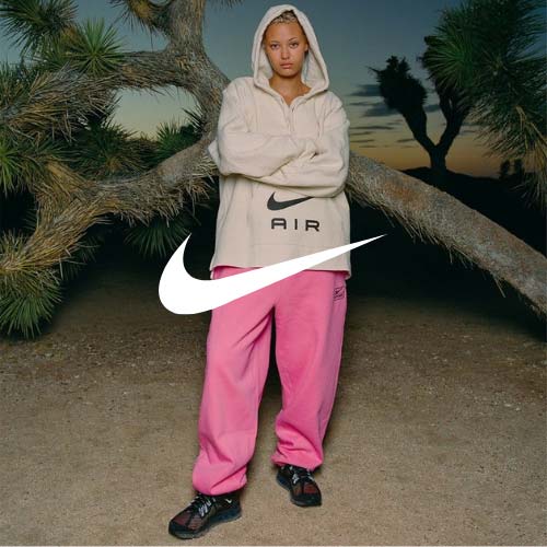 NIKE Logo, Frau mit rosa Joggingjhose, schwarzen nike air max, Nike air hoodie vor einem Hintergund in der Natur mit einem flach gewachsenen Baum