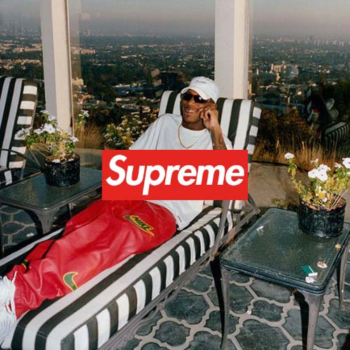 SUPREME Logo, Mann liegend auf eine Liege in roter Nike Supreme hose und weißem T Shirt mit einer Skyline im Hintergrund