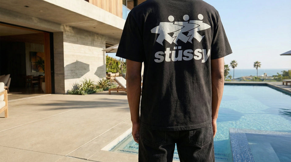 Stussy Logo mit einem mann in rosa Sweatshirt und schwarzer Hose vor einem Gebäude