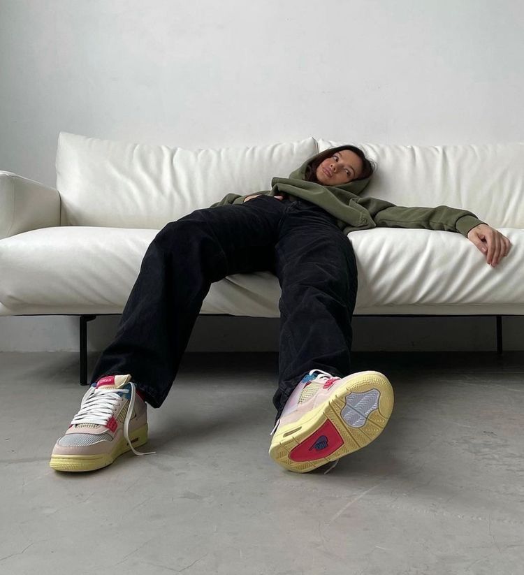 Frau liegend auf einer weißen Couch mit jordan Sneakern, schwarzer hose und grünem Pullover