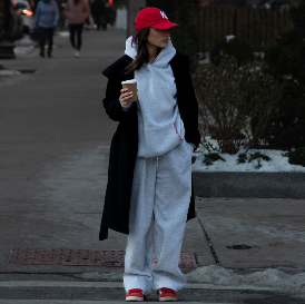Model mit roten Schuhen und Mütze mit grauem Sweater und Sweatpants steht an einer Kreuzung