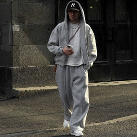 Model mit Sweathoodie und Sweatpants in grau mit weißen Air Force 1 und schwarzer Cap vor einem grauen Gebäude