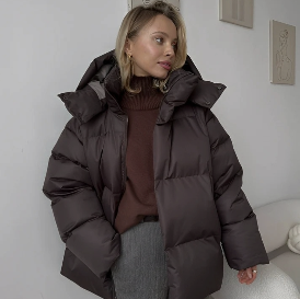 Model mit brauner Pufferjacket, braunem Rollkragen steht in einer Wohnung vor weißen Wänden