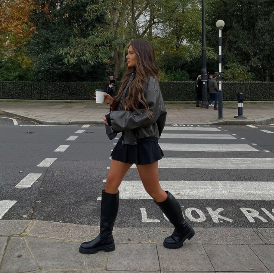 Model vor Zebrastreifen mit hohen schwarzen Stiefeln in schwarzem Minirock  und Lederjacke