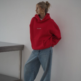 Model vor weißer Wand mit rotem Pullover und blauer Jeans