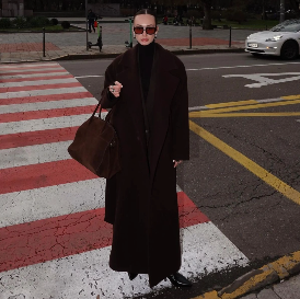 Model auf Zebrastreifen in langem schwarzen mantel mit dunkler Handtasche 