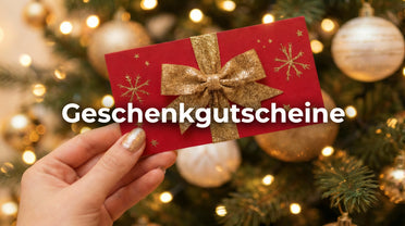 Geschenkgutscheine eine Hand mit golden lackierten Fingernägeln hält eine Geschenkkarte. Im Hintergrund steht ein Weihnachtsbaum