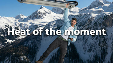 Heat of the moment, Mann in blauer Pufferjacke hängt an einem Skilift mit Bergkulisse im Hintergrund