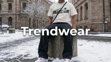 Trendwear, Mann in weißem Hellstar t-Shirt und Air Jordan Sneaker sitzt auf einem Stein vor verschneitem urbanen Hintergrund